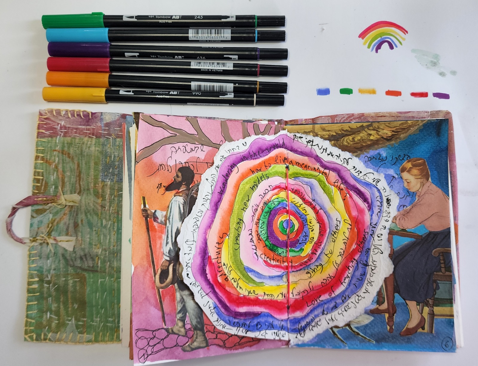 A torn paper circle painted in rings of color across a journal spread, with words written between the rings
