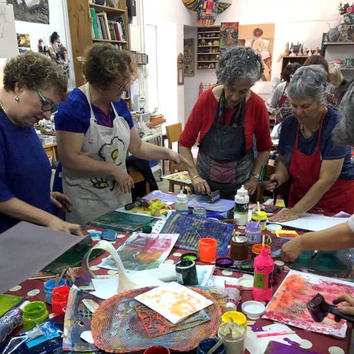 Women rolling paint onto printing plates at a shared table